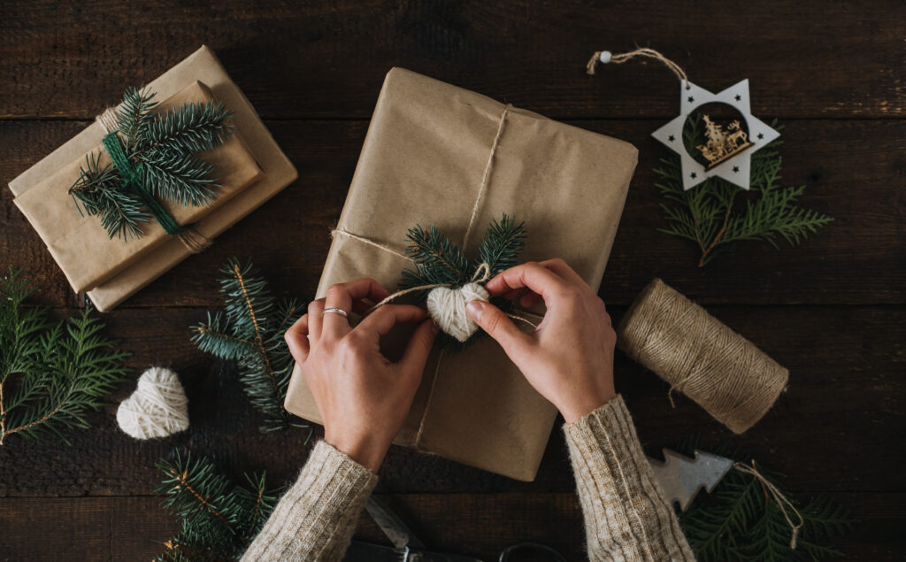 Giving Tuesday, Give, Help, Donation, Support, Volunteer concept with female hands wrapping craft gift box with knitted heart on wooden background.